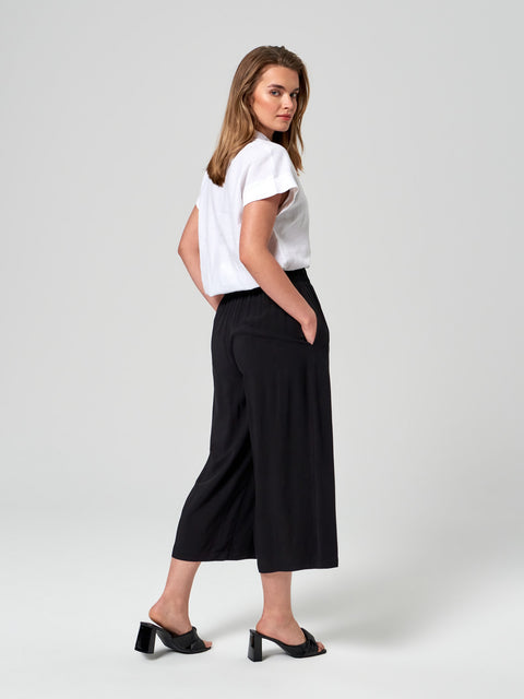 Woman wearing a white top and black wide-leg pants on a light gray background