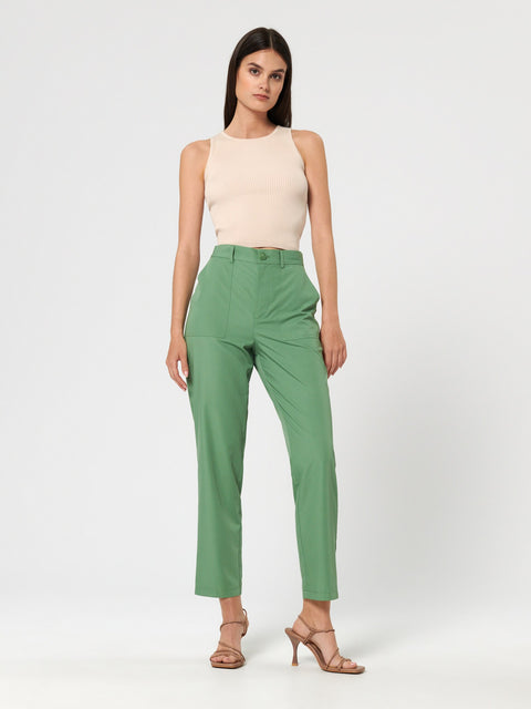 Woman wearing a beige sleeveless top and green pants on a white background