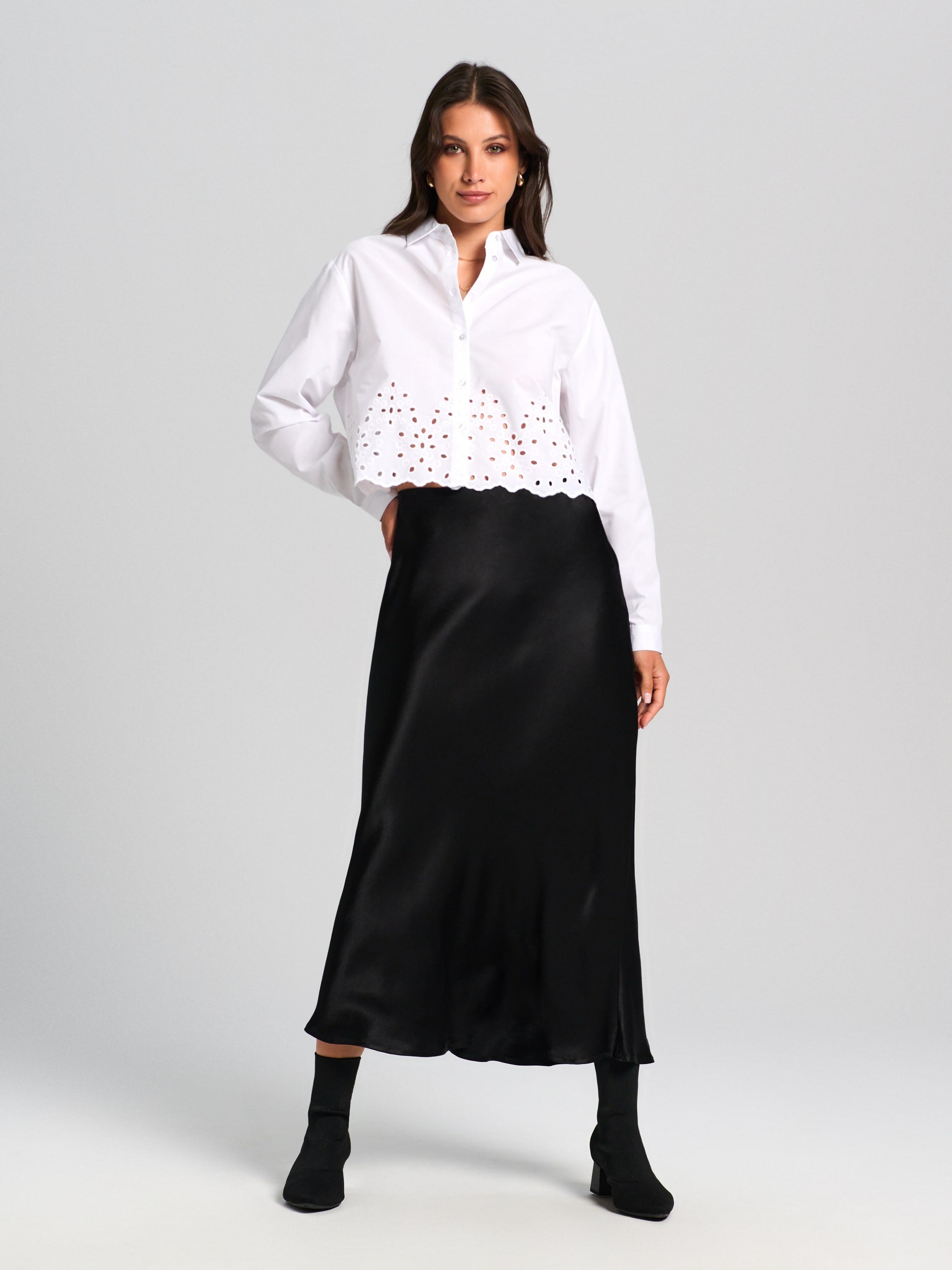 Woman wearing a white blouse with lace details and a black skirt on a gray background