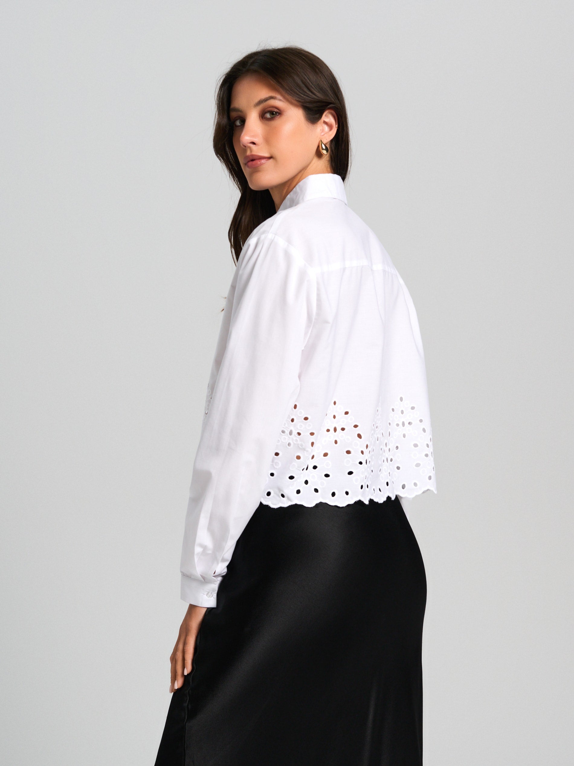 Woman wearing a white blouse with lace details on a gray background