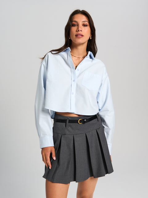 Woman wearing a light blue shirt and gray pleated skirt on a plain background