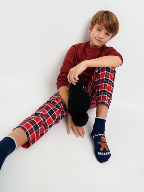 Child wearing red plaid pajama pants and dark socks with a gingerbread man design on a white background