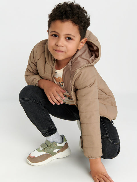 Child wearing a beige puffer jacket and dark jeans on a white background