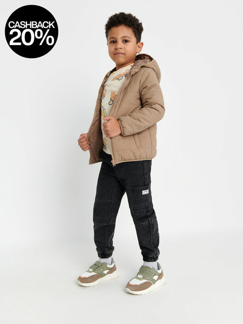 Child wearing a beige jacket, graphic t-shirt, black pants, and sneakers on a white background
