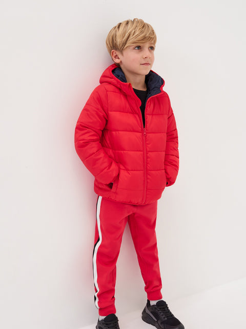 Child wearing a red puffer jacket and tracksuit against a white background