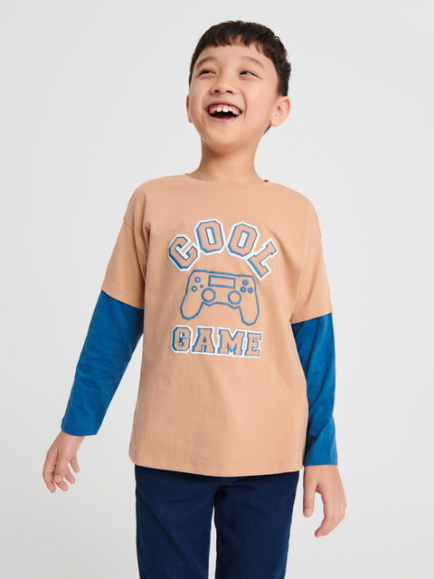 Child wearing a beige and blue long-sleeve shirt with 'Cool Game' text on a white background