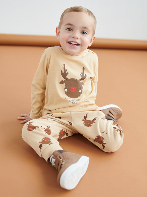 Child wearing a beige outfit with reindeer design on a brown background