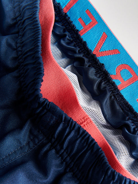 Close-up of navy and red swim trunks with a blue towel in the background.