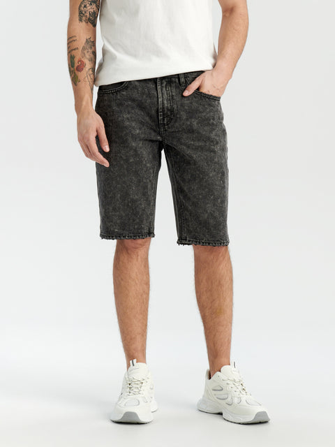Person wearing black denim shorts and white sneakers on a white background