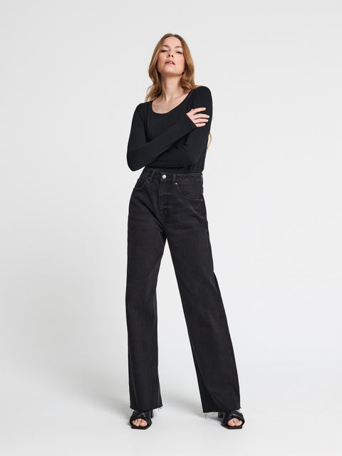Woman wearing a black outfit with high-waisted black jeans on a white background