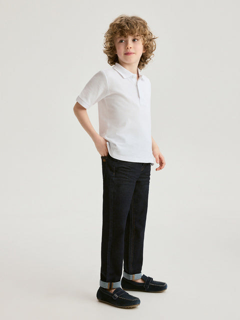 Child wearing a white shirt and black pants on a plain background