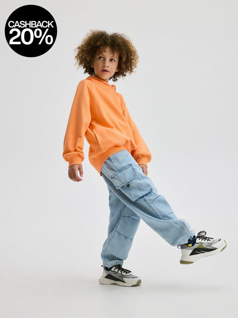 Child wearing an orange sweatshirt and blue cargo pants on a white background