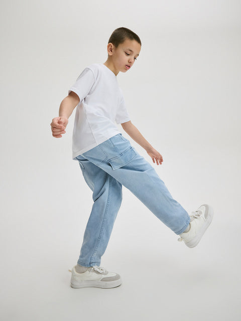 Child wearing a white t-shirt, light blue jeans, and white sneakers on a plain background
