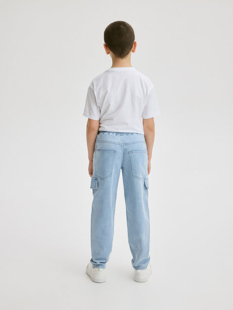 Child wearing light blue cargo pants and a white t-shirt on a plain background