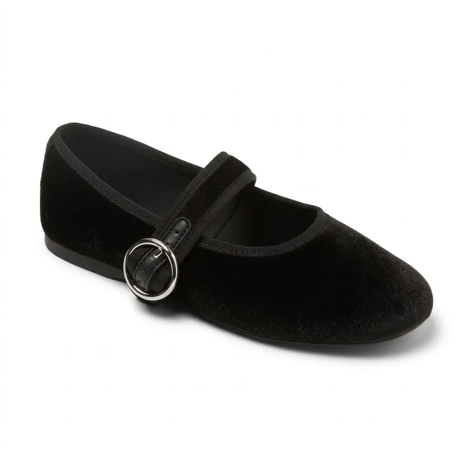 Black flat shoe with a strap and circular buckle on a light gray background