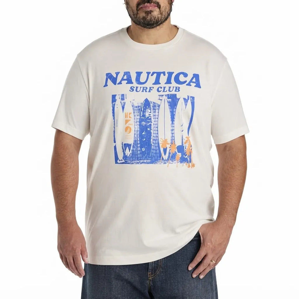 A man wearing a cream-colored Nautica Surf Club graphic t-shirt with blue and orange print, paired with dark blue jeans, against a plain white background.