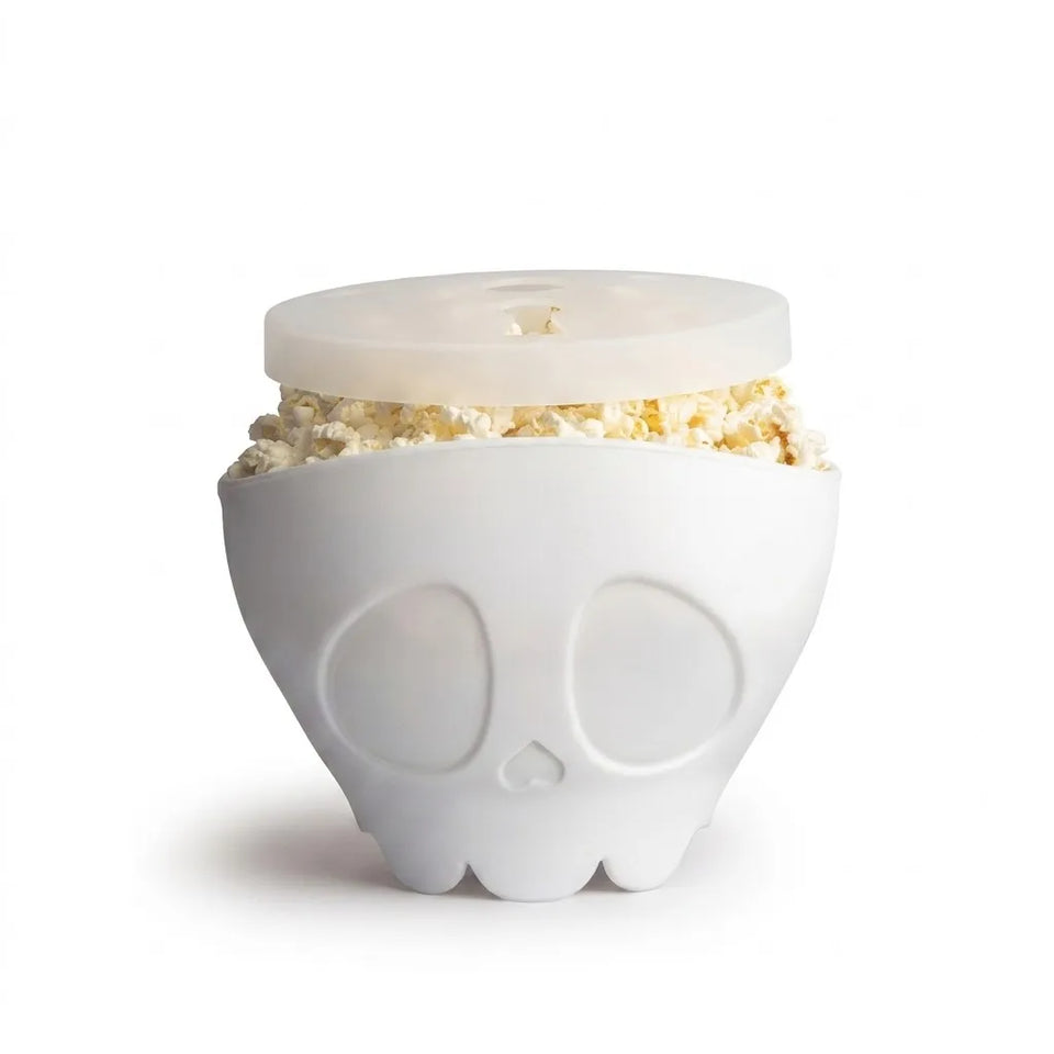 A white ceramic popcorn bowl shaped like a skull, filled with popcorn and topped with a translucent white lid, on a white background.
