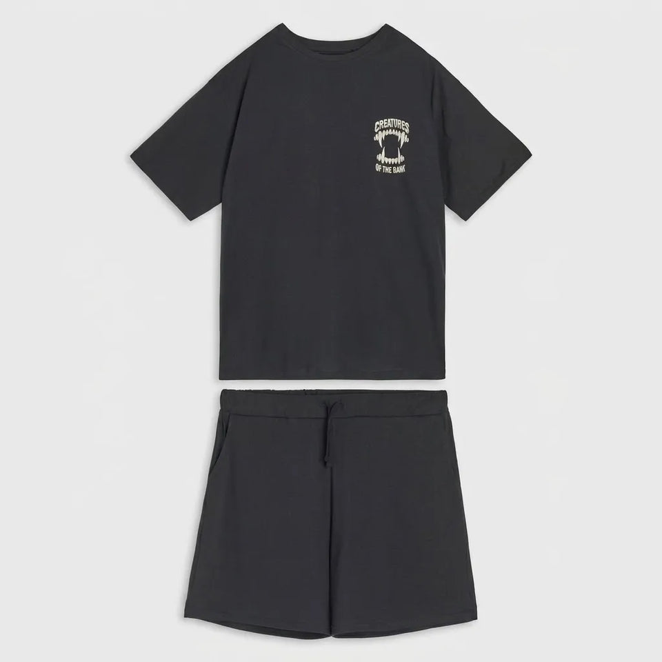 A two-piece kids' lounge set consisting of a black short-sleeve t-shirt with a small white graphic on the left chest and matching black shorts, displayed on a light gray background.