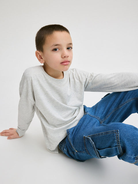 Child wearing a gray long-sleeve shirt and blue jeans sitting on a white surface.