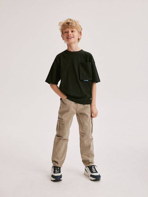Young boy wearing a black t-shirt and beige cargo pants on a white background