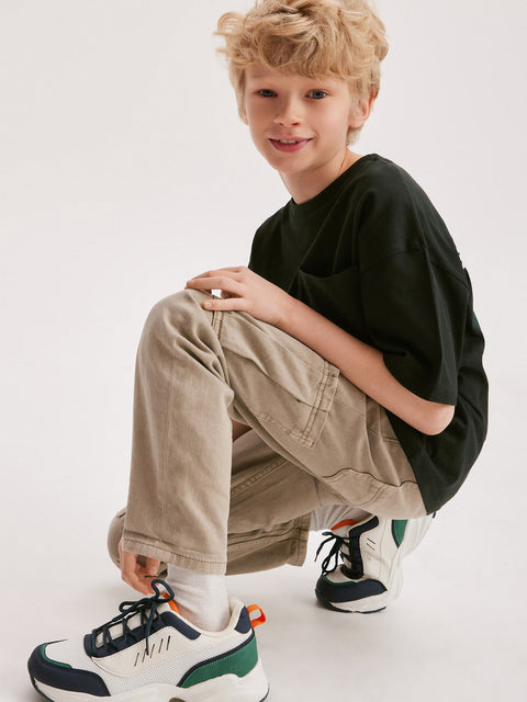 Young boy wearing a black oversized shirt, beige pants, and colorful sneakers on a white background