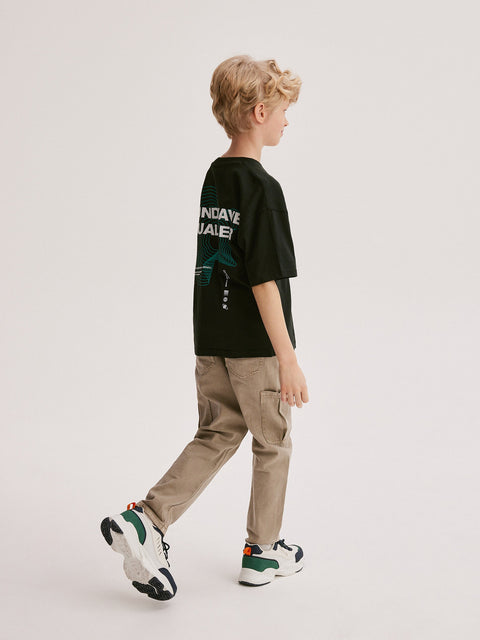 Child wearing a black t-shirt with text and graphics, beige pants, and colorful sneakers on a white background