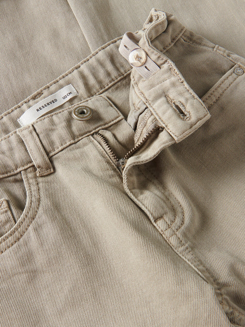 Close-up of beige pants with a button and label visible.
