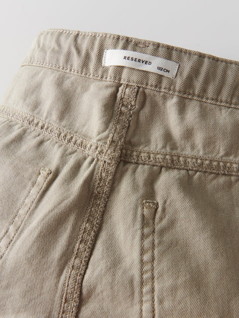 Close-up of beige pants with a 'RESERVED' label on a light gray background