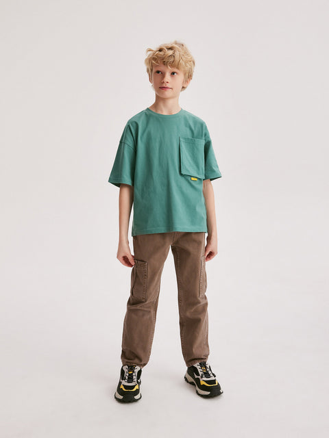 Young boy wearing a green t-shirt and brown pants on a white background