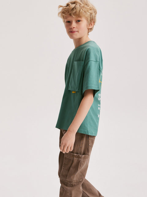 Child wearing a green t-shirt and brown pants on a white background