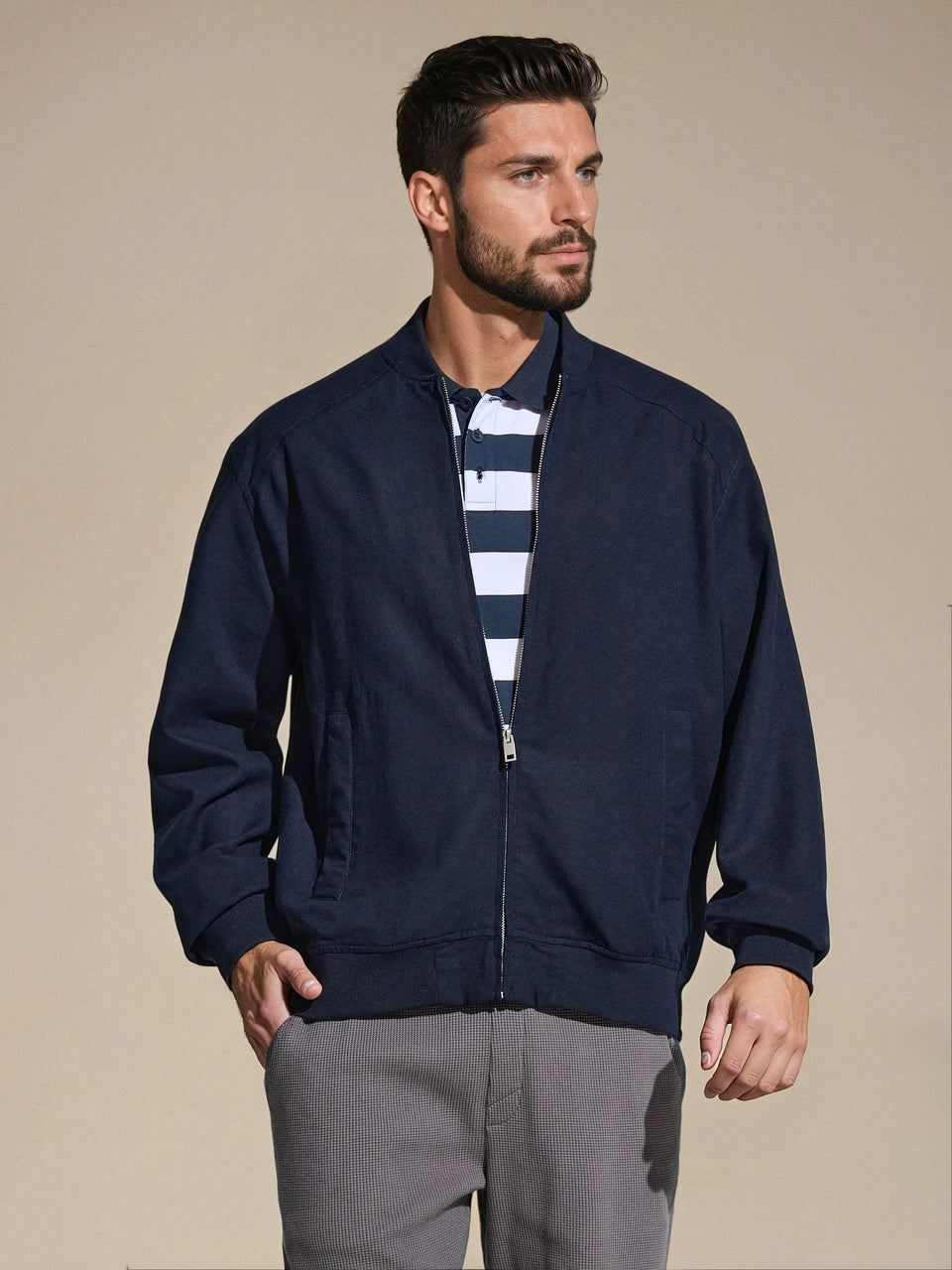Man wearing a navy bomber jacket over a striped shirt on a beige background