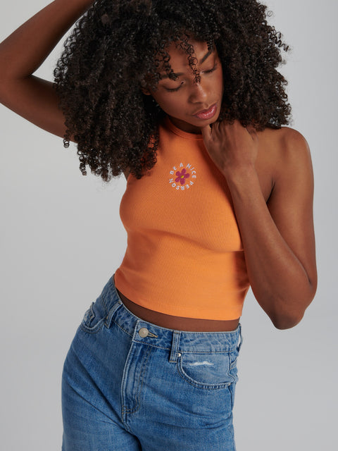 Woman wearing an orange tank top with a floral design and blue jeans on a plain background