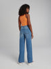Person wearing an orange tank top and blue jeans on a plain background