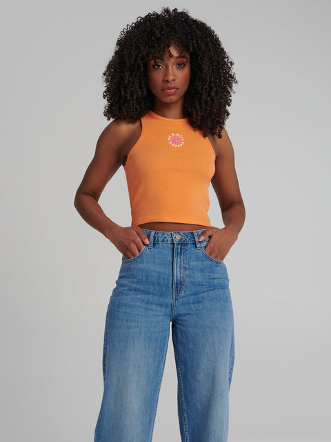 Woman wearing an orange tank top and blue jeans against a gray background