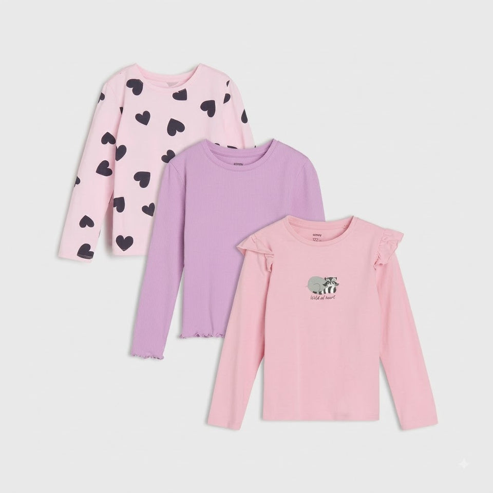 Three girls' long-sleeve tops in pink and lavender shades, displayed in a layered flat-lay arrangement on a light gray background. The top-left shirt is light pink with black heart prints, the middle shirt is lavender, and the bottom-right shirt is light pink with ruffled shoulders and a small elephant graphic on the chest.
