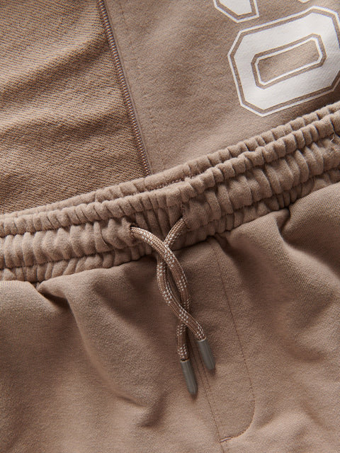 Close-up of brown sweatpants with a drawstring and number '8' on a beige background