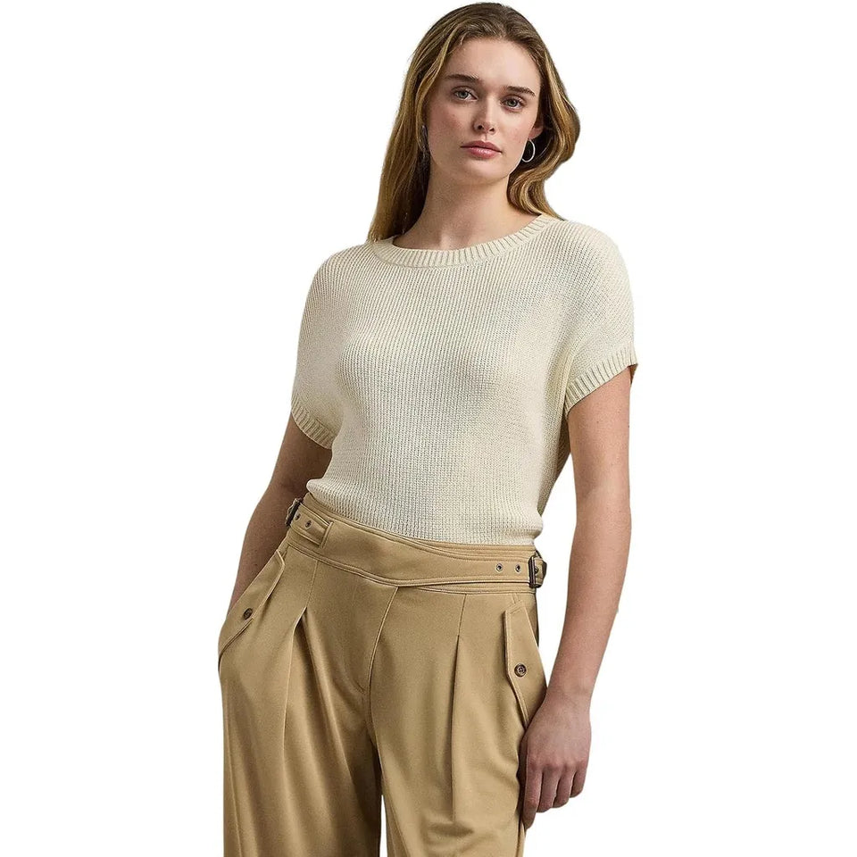 A woman modeling a short-sleeve ribbed knit sweater in cream, paired with tan high-waisted trousers, against a plain white background.