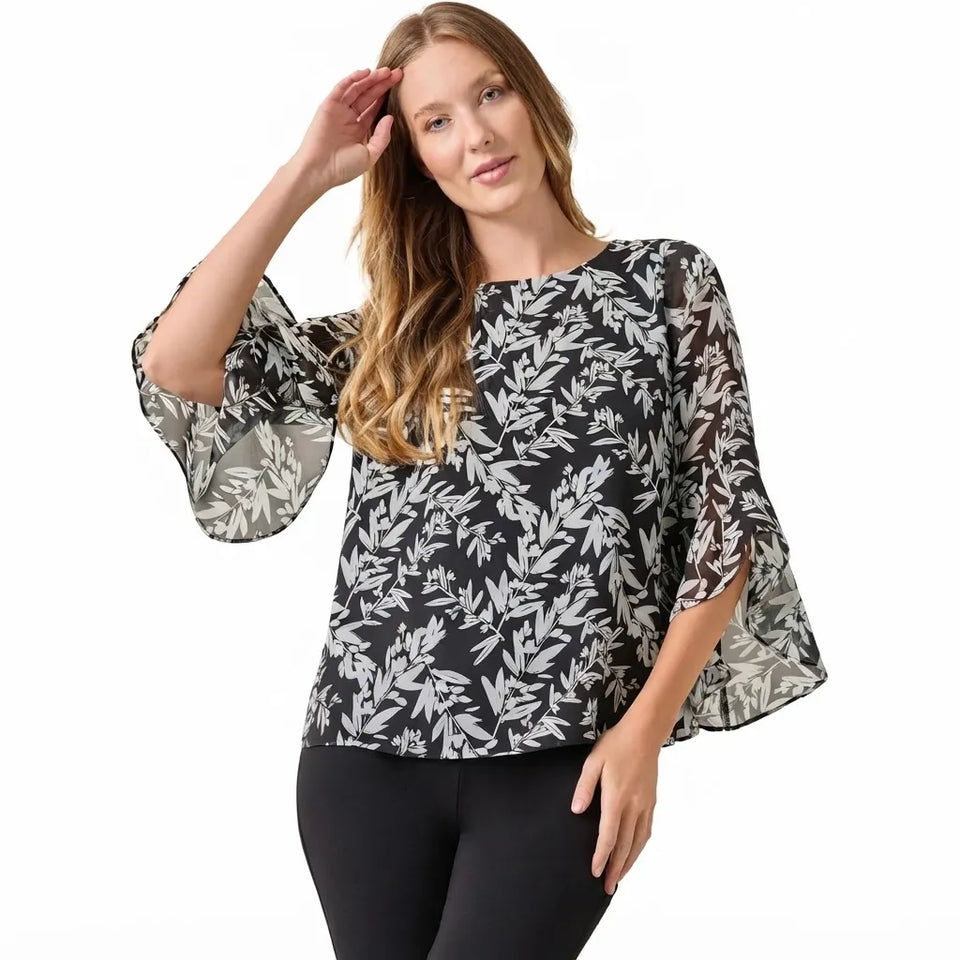 A woman modeling a black blouse with a white leaf pattern and flared bell sleeves, paired with black pants, against a plain white background.