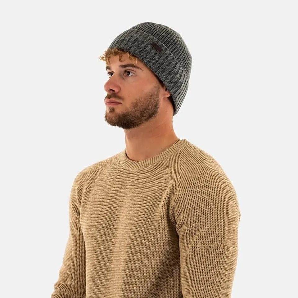 A man wearing a dark gray ribbed knit beanie and a tan ribbed knit crewneck sweater, shown in profile against a light gray background.