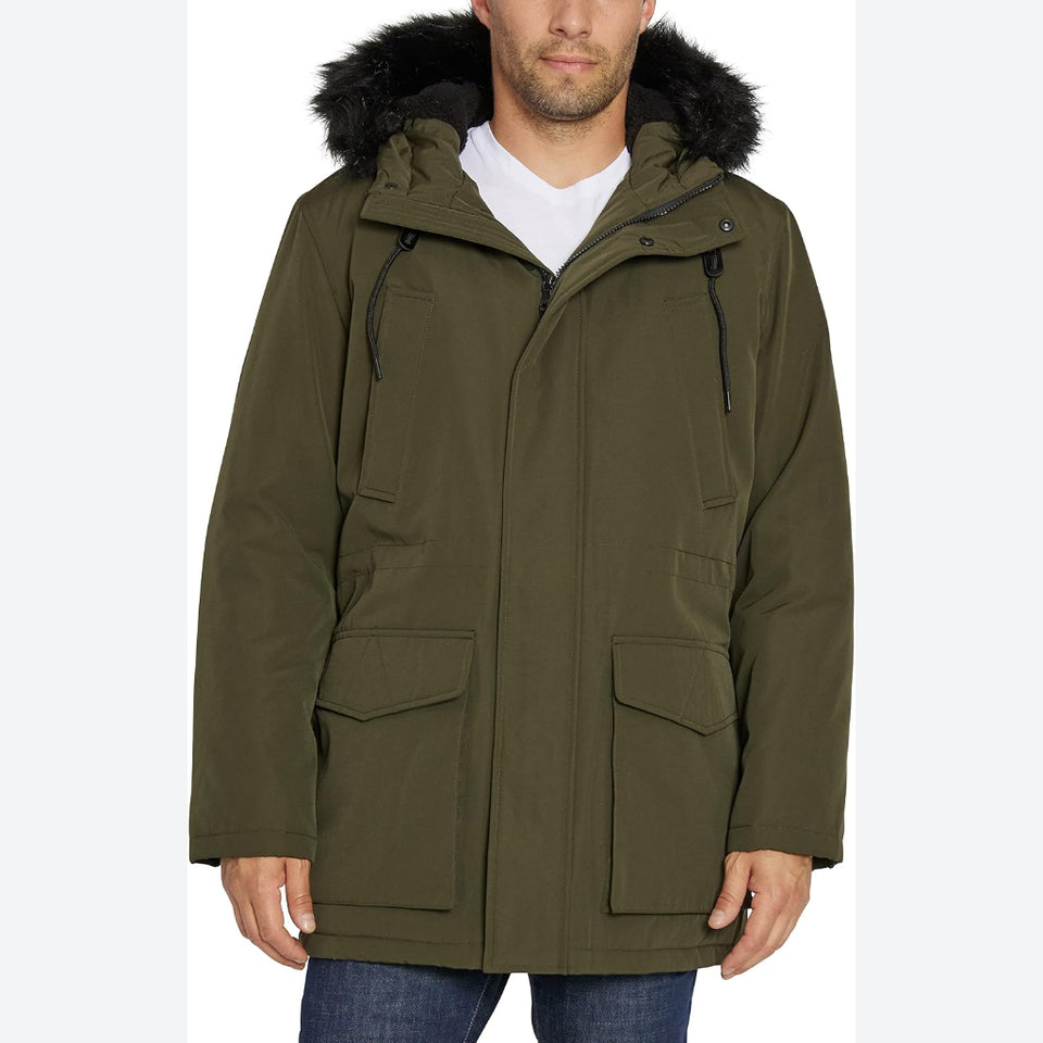 An olive green hooded parka jacket with black faux-fur trim on the hood, worn by a model over a white t-shirt and blue jeans against a light gray background.