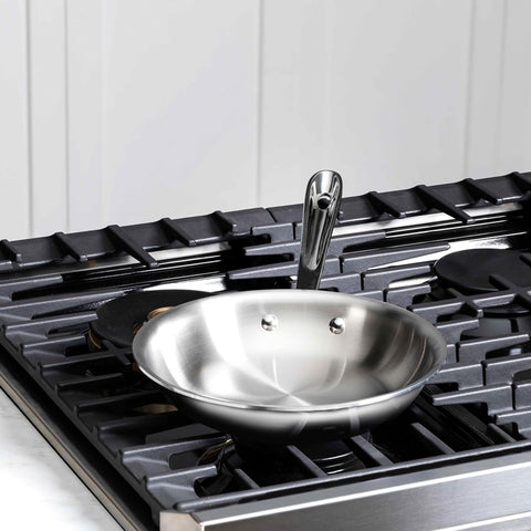 Stainless steel frying pan on a gas stove with a white tiled wall background