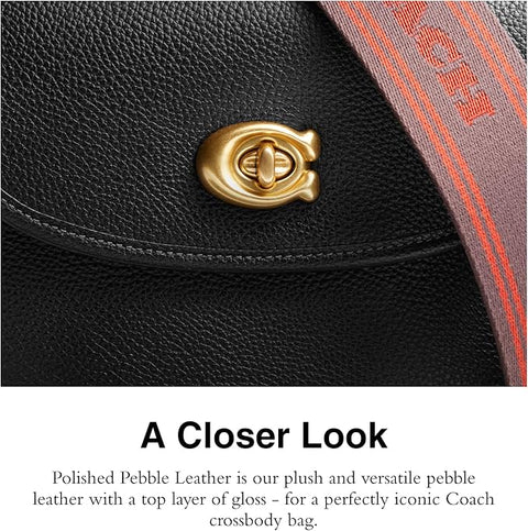 Close-up of a black Coach crossbody bag with gold clasp and red strap.