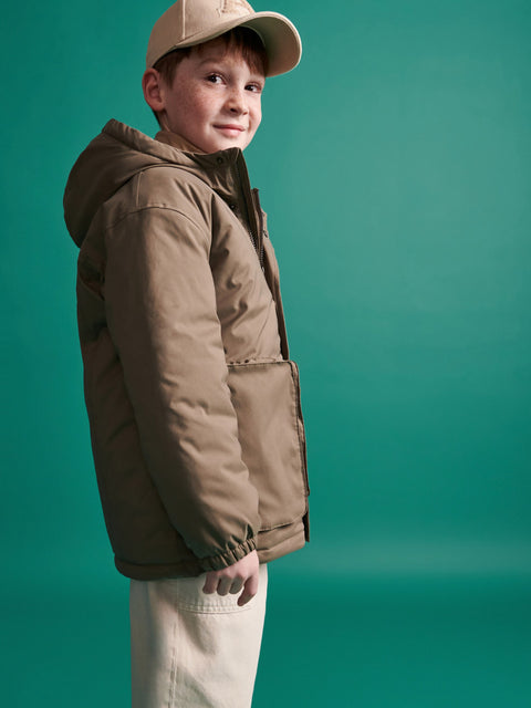 Child wearing a brown jacket and cap against a teal background