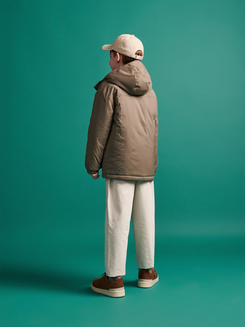 Person wearing a brown puffer jacket and beige cap on a teal background