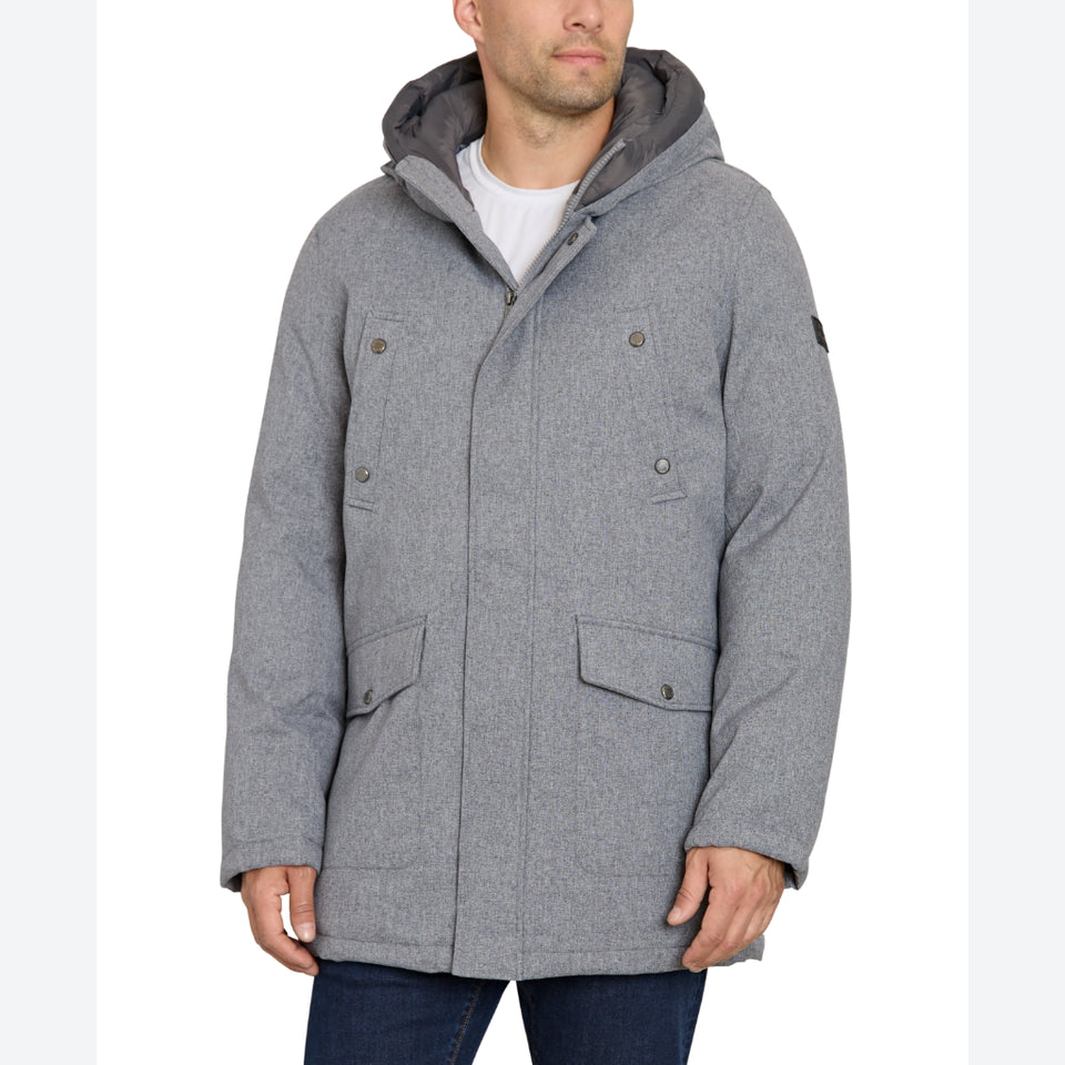 A man wearing a heather gray hooded winter parka jacket with flap pockets and snap details, paired with a white t-shirt and dark blue jeans, shown against a plain white background.