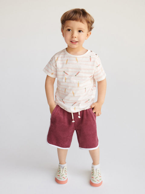 Child wearing a patterned shirt and maroon shorts on a white background