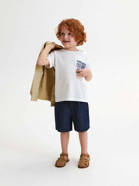 Child wearing a white t-shirt with a graphic design, navy shorts, and brown sandals on a white background