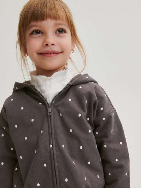 Child wearing a gray hoodie with white polka dots on a plain background