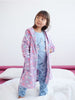 Young girl in a pink heart-patterned robe and blue pajama set on a white bed.