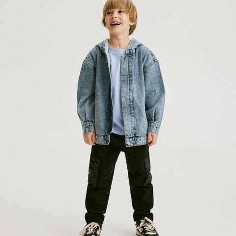 Child wearing a denim jacket, white shirt, black pants, and sneakers on a light gray background